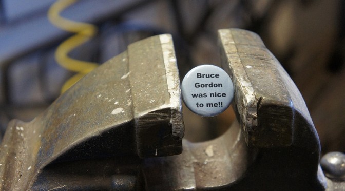A blue button that says "bruce gordon was nice to me," clamped lightly in a vice.